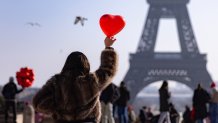 A woman holds up a red heart-shaped balloon on the Esplanade du Trocadero near the Eiffel Tower on the Valentine's Day in Paris on February 14, 2025. (Photo by Ian LANGSDON / AFP) (Photo by IAN LANGSDON/AFP via Getty Images)