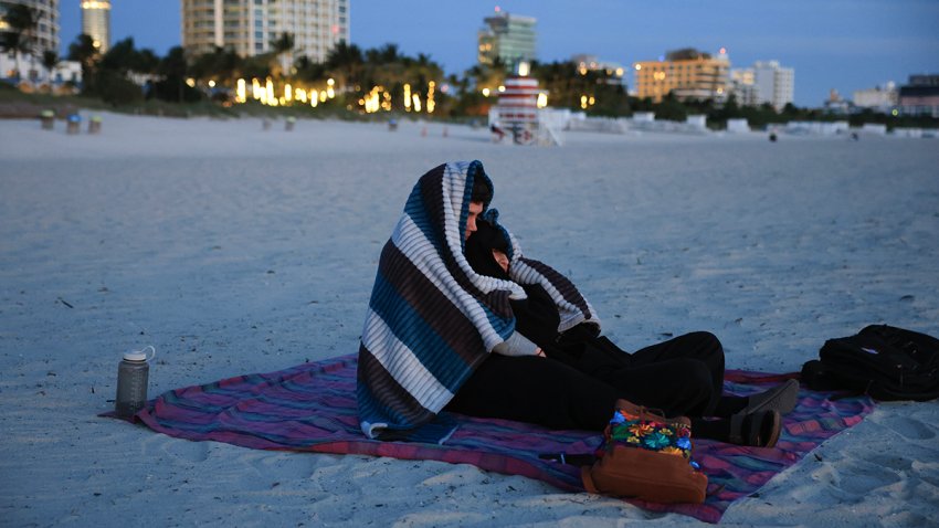MIAMI BEACH, FLORIDA – NOVEMBER 11: Two people (who did not want to provide their names) bundle up against the chilly air as they watch the sunrise on the beach on November 11, 2025 in Miami Beach, Florida. A cool blast of air moved through the area in the morning with temperatures in the upper-40s all across South Florida, and with wind chill it was in the low- to mid-40s. (Photo by Joe Raedle/Getty Images)