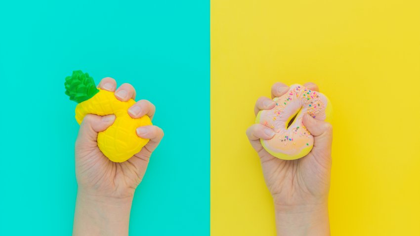 Flat lay antistress squish toys yellow pineapple,pink donut with sprinkles in hands.Bright blue background.Compressing,soft,squeezable items to relieve stress,problem,anxieties,worries.Summer concept.