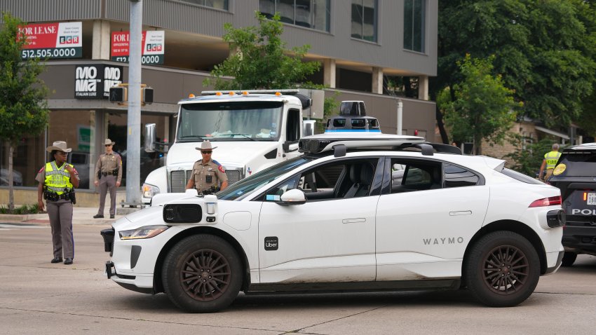 Texas Department of Public Safety troopers watch a Waymo robotaxi pass through the intersection near a rollover crash at West 15th and San Antonio streets in Austin on Tuesday, May 26, 2026.